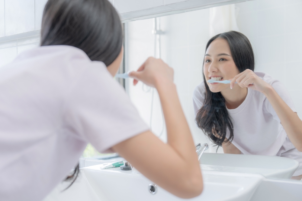Smiling,Young,Asian,Woman,Brushing,Teeth,In,Bathroom.